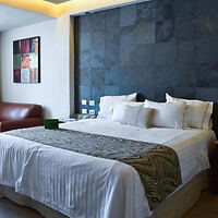 Contemporary room at Hotel Portobelo with a large bed featuring white linens, a geometric patterned throw, a dark stone accent wall, and abstract art