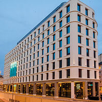 Exterior view of Motel One in the evening with its illuminated facade, showcasing modern architecture with a curved corner design