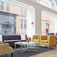 Stylish lobby with bold yellow armchairs, a chic patterned sofa, and large arched windows offering a view of the street