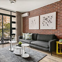 A comfortable living area in an Easy Stay apartment, displaying a gray sofa, a brick accent wall, white coffee tables, and abstract art