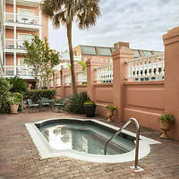 Courtyard at the Meeting Street Inn showing a small, tranquil plunge pool surrounded by pink walls, potted plants, and a classic Charleston piazza in the background