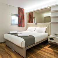 Compact modern hotel room with striped curtains and wooden flooring