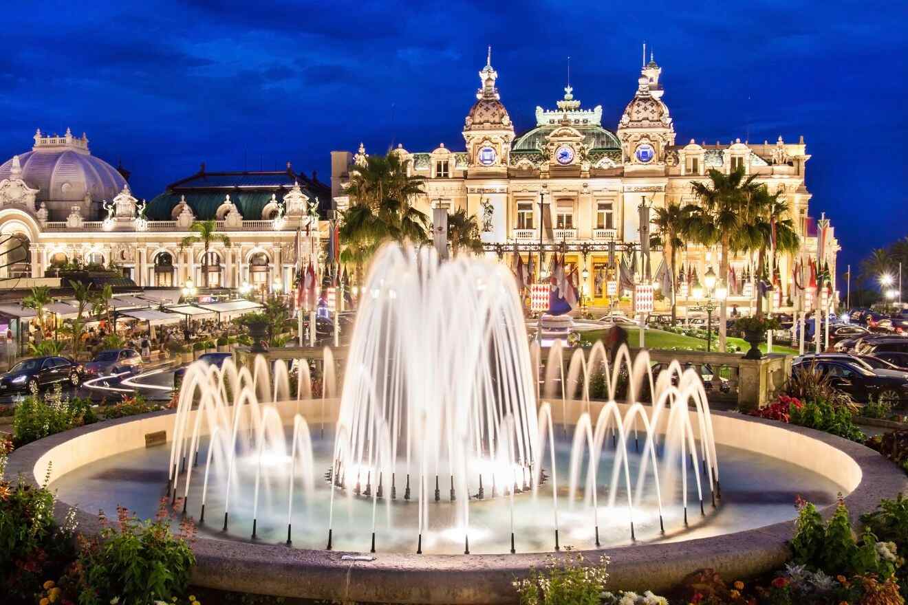 Twilight view of the opulent Monte Carlo Casino, illuminated against the night sky, with a vibrant fountain in the foreground
