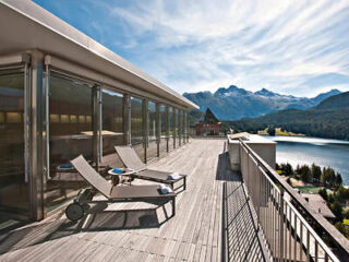 Large wooden deck with lounge chairs overlooking a stunning mountain lake
