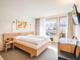 Hotel room with wooden bed frame, colorful art, and mountain view.