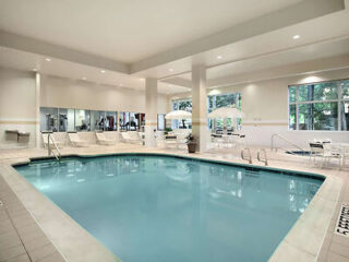 Indoor hotel pool with surrounding loungers and large windows offering natural light