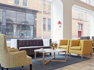 Contemporary hotel lounge with a mix of patterned armchairs, a mustard yellow sofa set, and a brown tufted bench, creating a vibrant yet sophisticated waiting area with large windows
