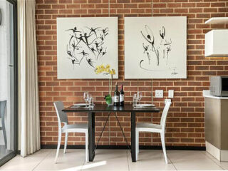 Contemporary dining space in an Easy Stay apartment featuring a dining table set for two, a brick wall backdrop, and abstract monochromatic art, giving the room an artistic flair