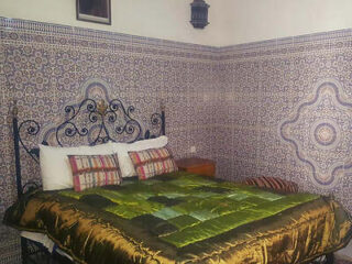 Cozy Moroccan bedroom featuring intricate tile work, a wrought-iron bed frame, and lush green and gold bedding
