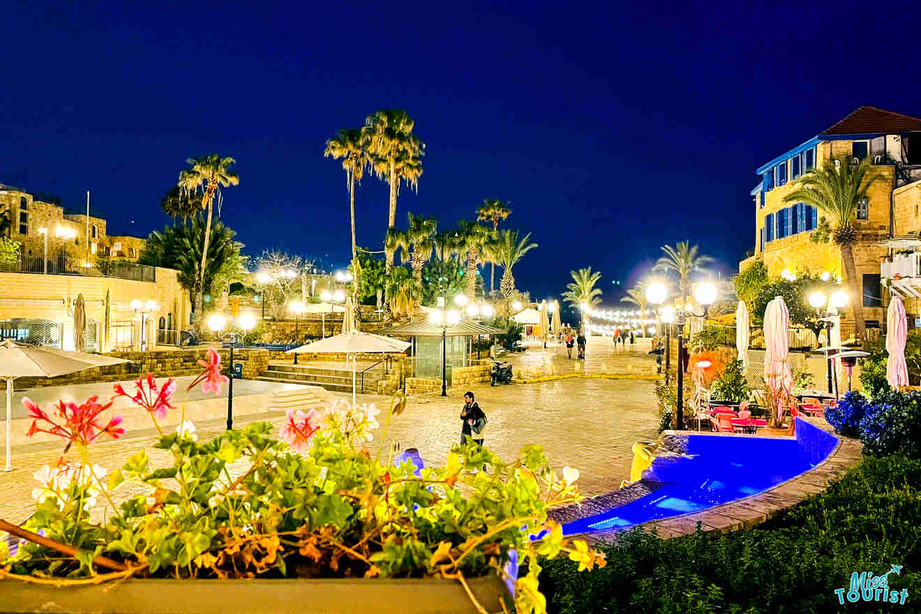 An evening view of Jaffa Square, with bright streetlights illuminating the historic architecture and a tranquil pool in the foreground