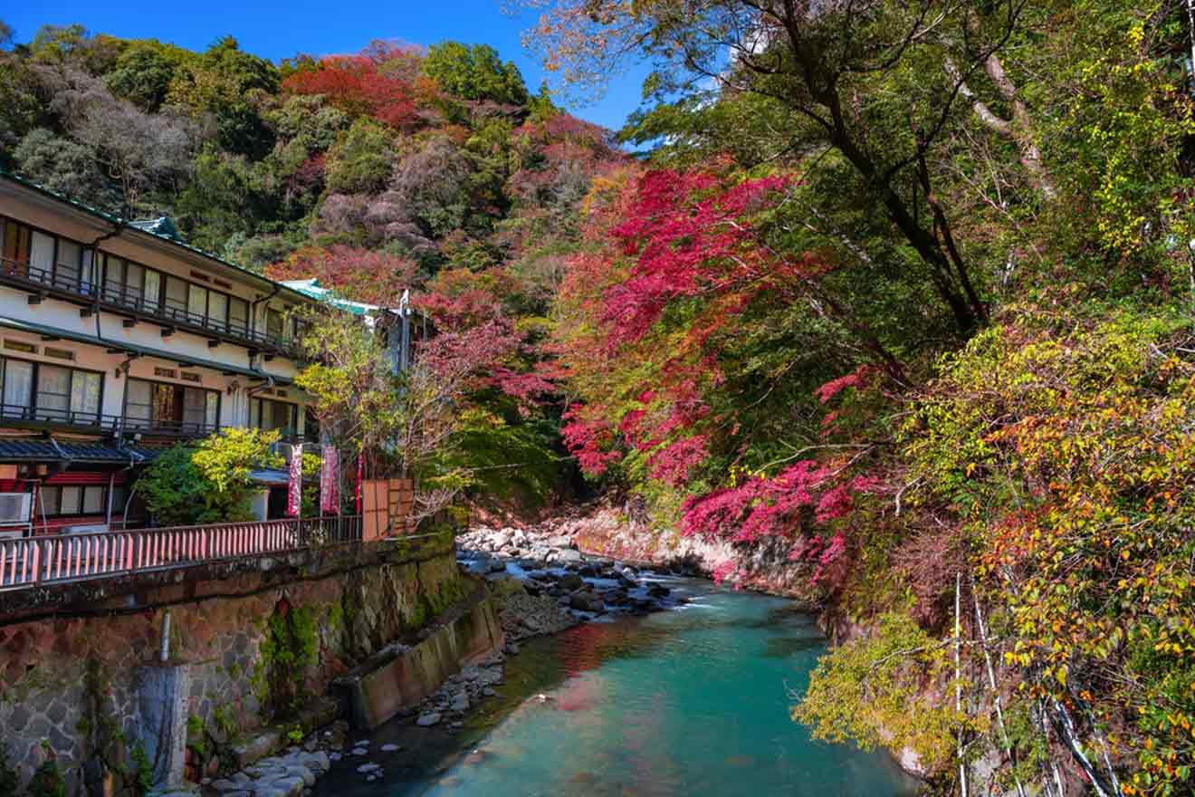 A serene view of Hakone Yumoto, showcasing the vibrant autumn foliage with shades of red, yellow, and green surrounding a tranquil river that flows by traditional Japanese inns.