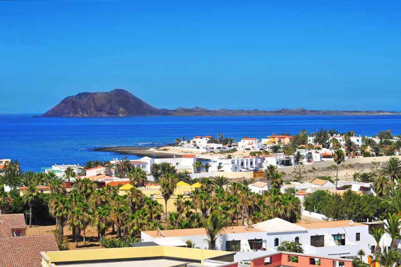 Overlooking view of Corralejo in Fuerteventura featuring white buildings against a backdrop of an azure sea and a volcanic island.
