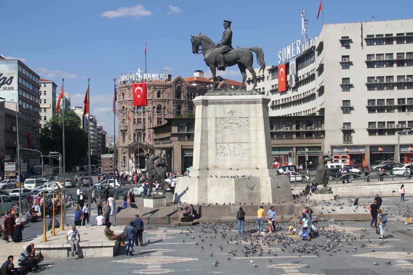 A bustling city square in Ankara, with a statue of Atatürk on horseback at its center, surrounded by pedestrians, pigeons, and historic buildings with Turkish flags.
