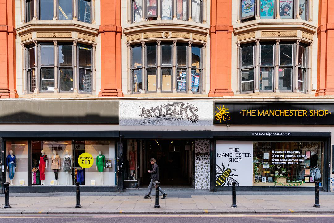 Afflecks and The Manchester Shop storefronts on a vibrant Manchester street, showcasing a mix of fashion items and local merchandise