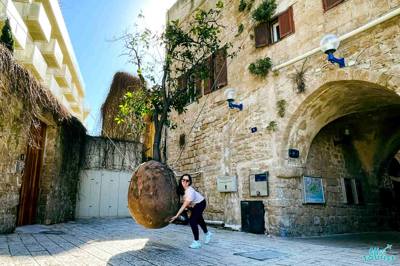 The author of the post engaging with a suspended rock art installation in the stone-paved alleyways of Jaffa's historical quarter.
