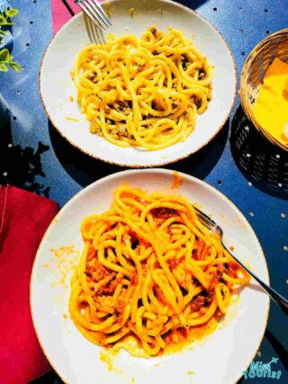 Two plates of spaghetti with meat sauce served on a blue tablecloth, capturing the essence of Padua's street food and local delicacies