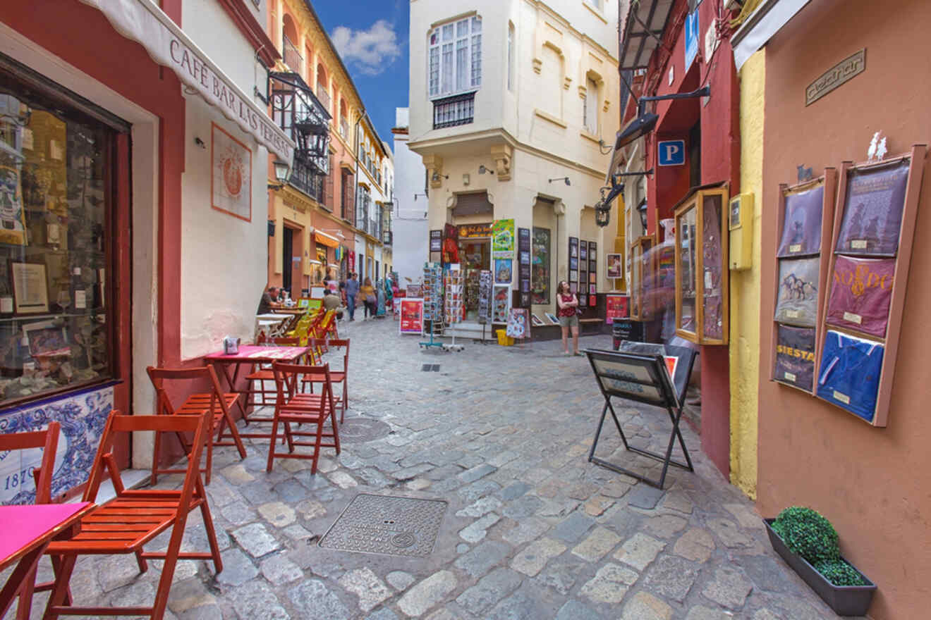 A picturesque view of a quaint alley in the Santa Cruz district, lined with colorful buildings, outdoor cafes, and cobblestone streets