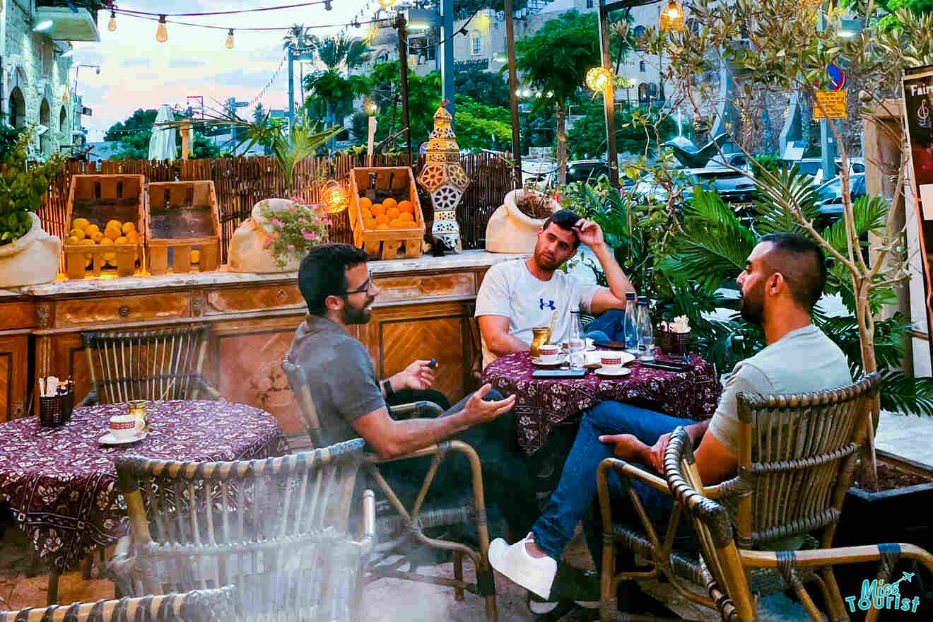 A lively evening scene at a Jaffa café, with guests enjoying beverages amidst a rustic and decorative setting