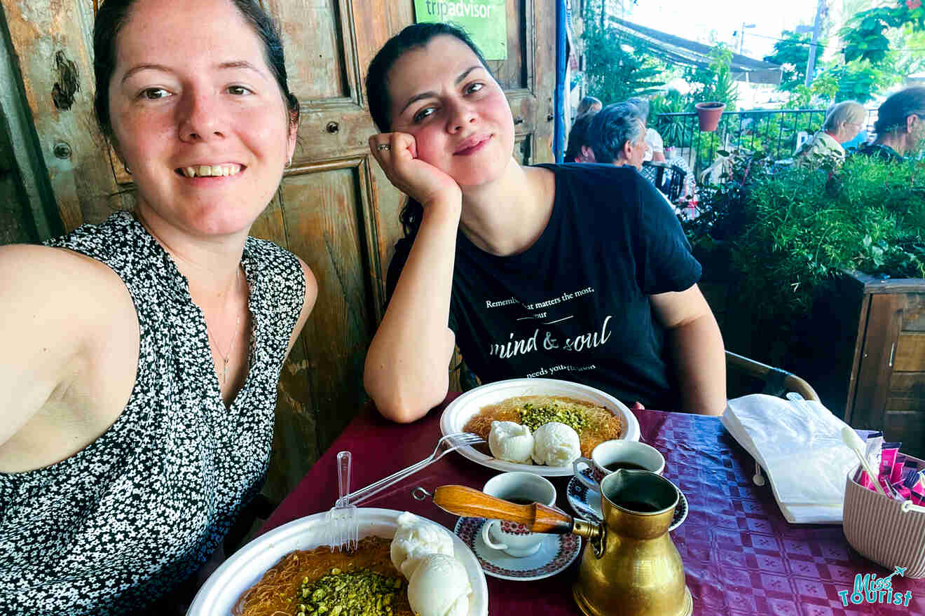 The author of the post with her friend sitting at a table with Middle Eastern cuisine, including kunafa and ice cream, in a vibrant cafe setting