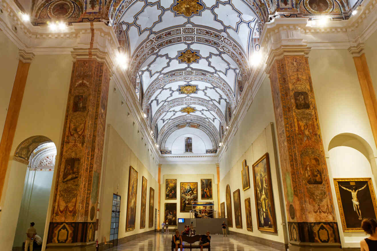 An opulent interior of the Museo de Bellas Artes, featuring intricate ceiling designs and an extensive collection of fine art pieces along the walls