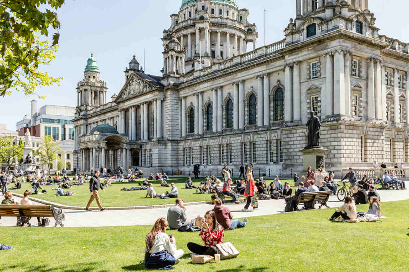 People enjoying a sunny day in front of the historic Belfast City Hall with its stunning architecture and manicured lawns.