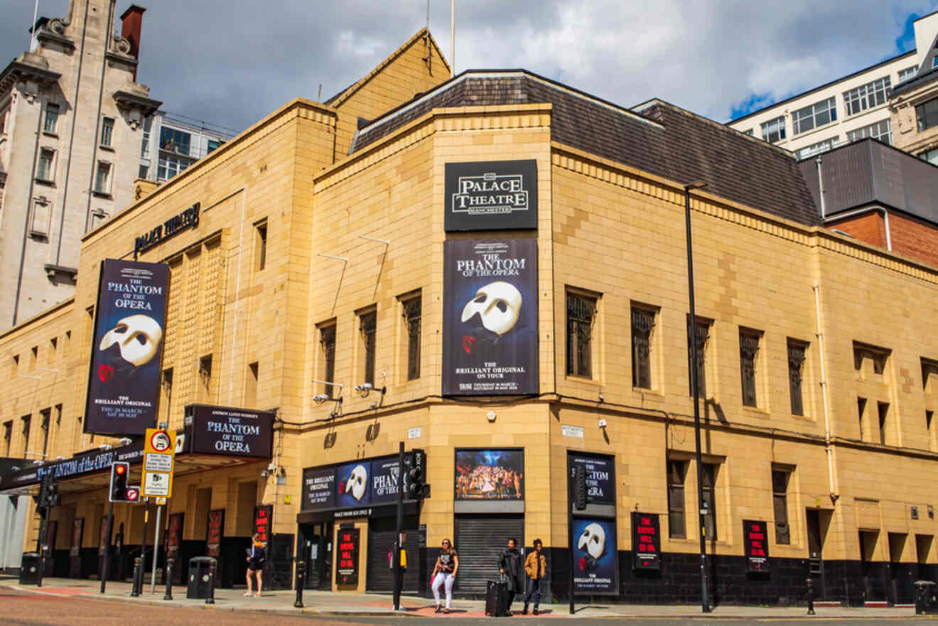 The Palace Theatre in Manchester during the day, with banners for "The Phantom of the Opera" adorning its classic yellow-brick façade.