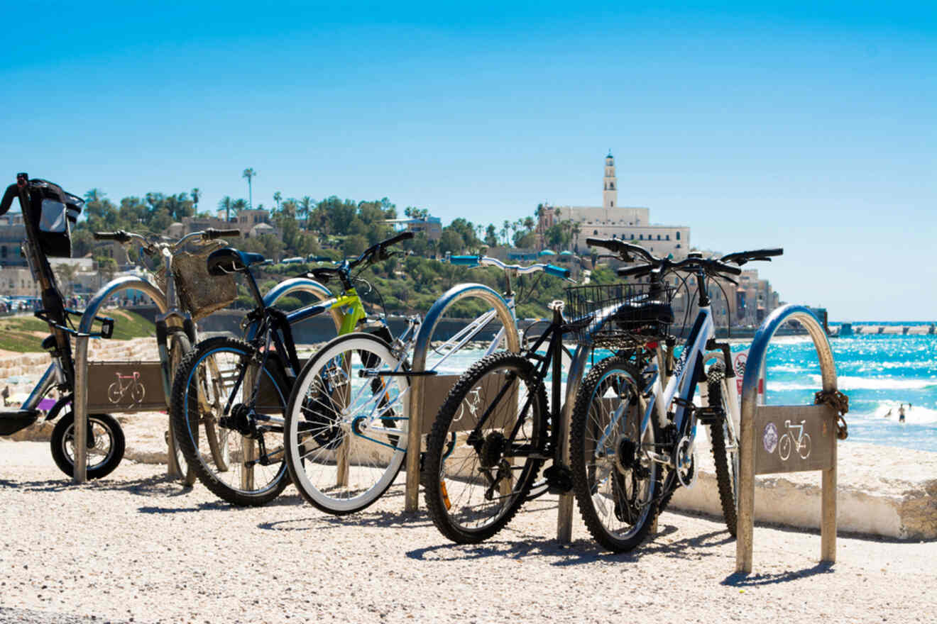 Bicycles parked on a sandy beach with a clear view of the ocean and a historic tower in the distance