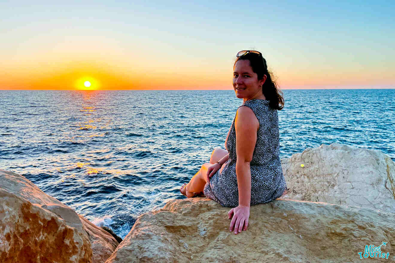 The author of the post sitting on a rocky shore enjoying a stunning sunset over the Mediterranean Sea in Jaffa, Tel Aviv, with the horizon glowing in warm hues