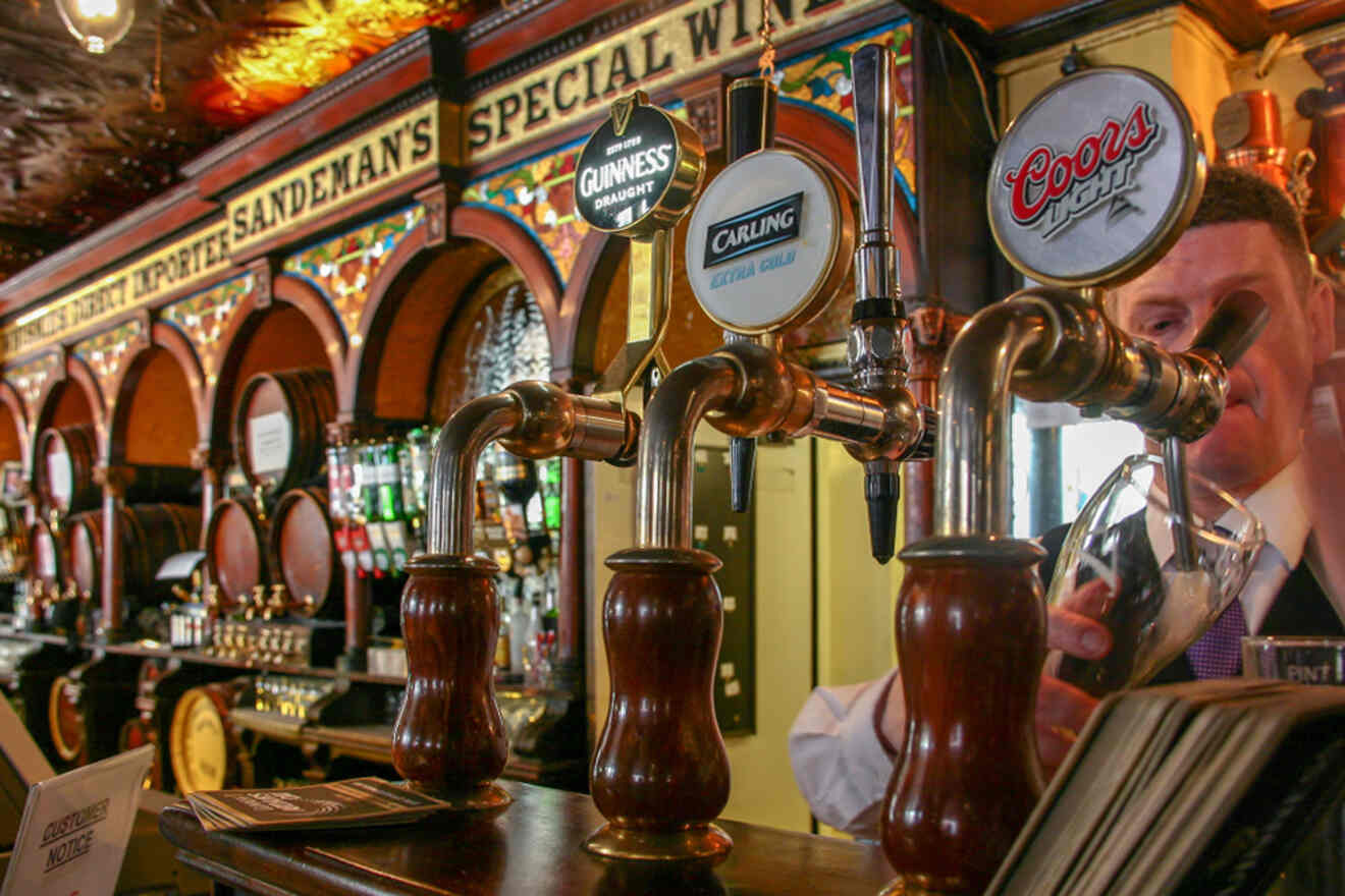 Traditional beer taps at Belfast's Crown Liquor Saloon with a bartender serving a pint.