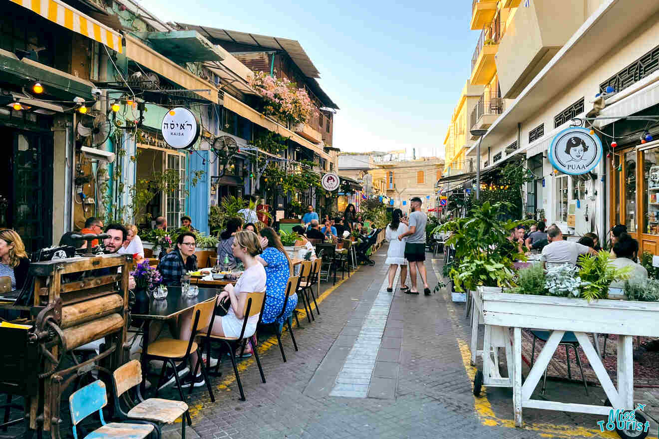 Bustling street view of Jaffa with diners at outdoor cafes, vibrant storefronts, and string lights adding a cozy ambiance to the historic neighborhood