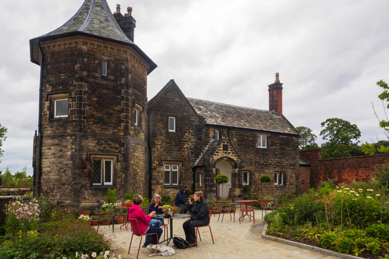 A group of people enjoying a casual outdoor gathering at a rustic garden setting in front of an old stone building with lush greenery