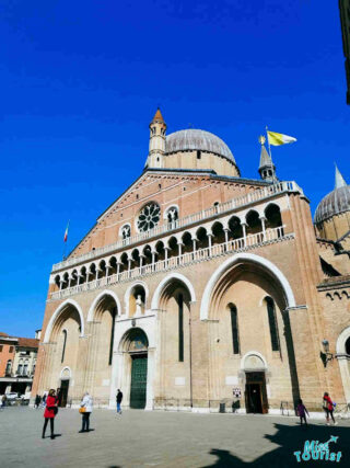 Exterior facade of the Basilica of Saint Anthony of Padua against a clear blue sky, with people exploring the spacious square