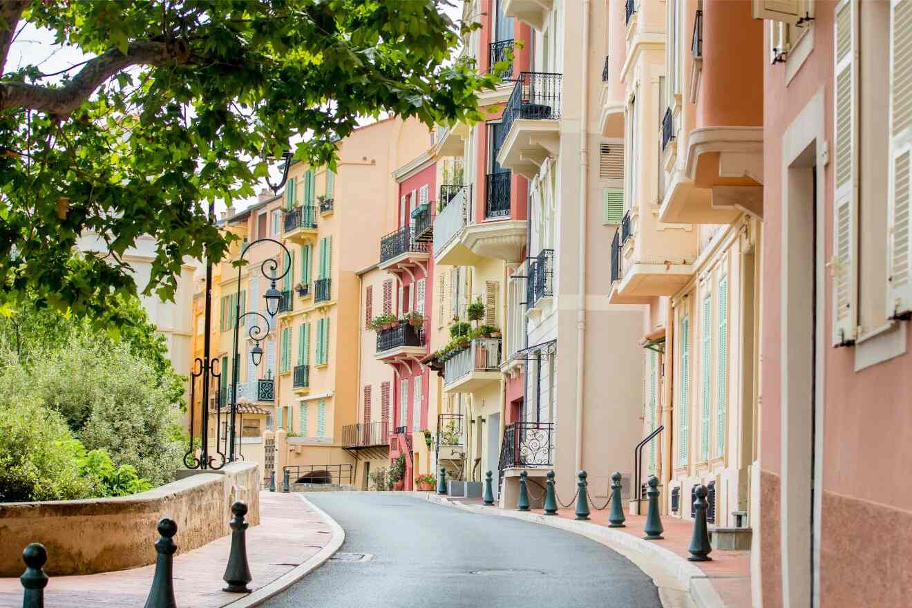 Charming pastel-colored buildings line a curved street in Monaco-Ville, flanked by green trees and ornate street lamps