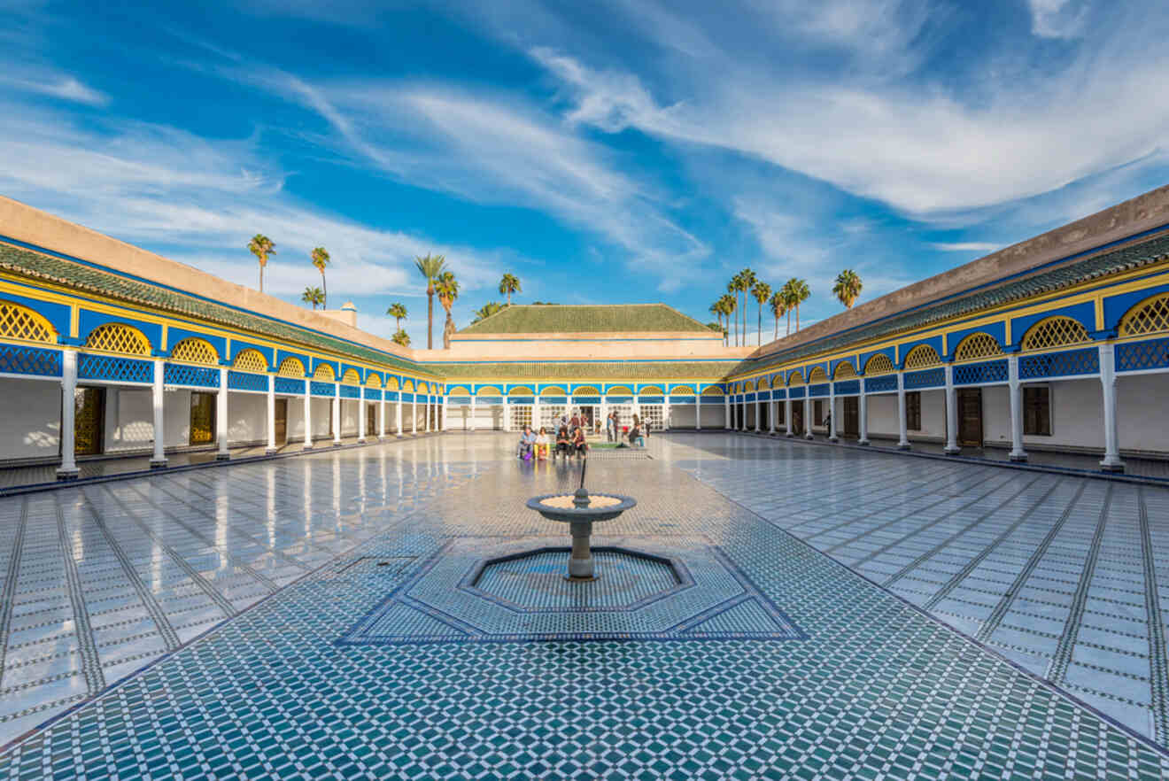 Expansive courtyard of Bahia Palace in Marrakech, featuring intricate Moroccan tile work, vibrant blue and yellow architectural details, and a serene fountain, under a clear blue sky