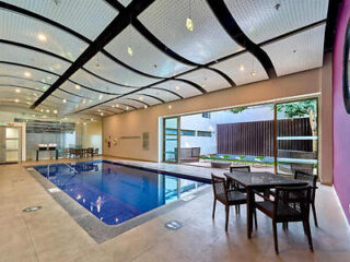 Indoor hotel pool under a curved ceiling with dining tables nearby, creating an inviting space for relaxation