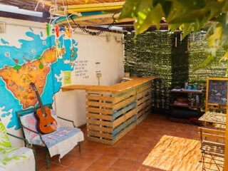 Cozy outdoor terrace of Arena Nest Hostel with world map mural, guitar, and upcycled wooden pallet furniture under a shaded patio