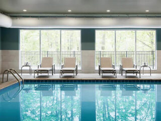 Indoor pool at Avid, an IHG Hotel, featuring tranquil blue waters and relaxing lounge chairs, with natural light filtering through floor-to-ceiling windows
