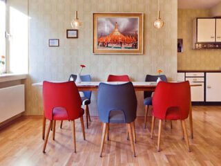 A cozy dining area in Hostel die Wohngemeinschaft featuring colorful chairs, a wooden table, and a vibrant picture of a cathedral on the wall