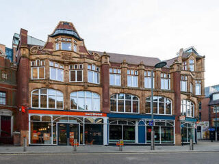 Historic red and tan brick building with large windows on Waterloo Street, housing an easyHotel and retail outlets, under a clear blue sky