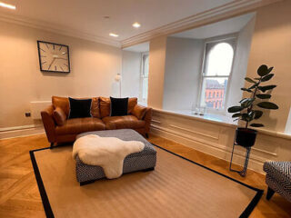 Comfortable living room with a tan leather couch, plush white rug, and large windows in an upscale apartment setting
