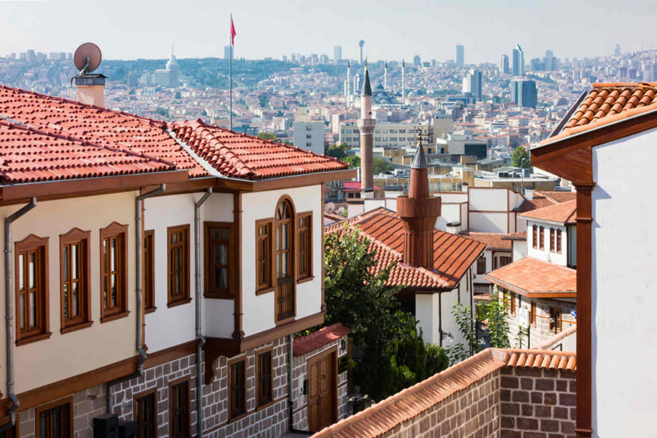 Traditional Ottoman houses with red-tiled roofs in the old quarter of Ankara, with the modern cityscape and a Turkish flag in the distance