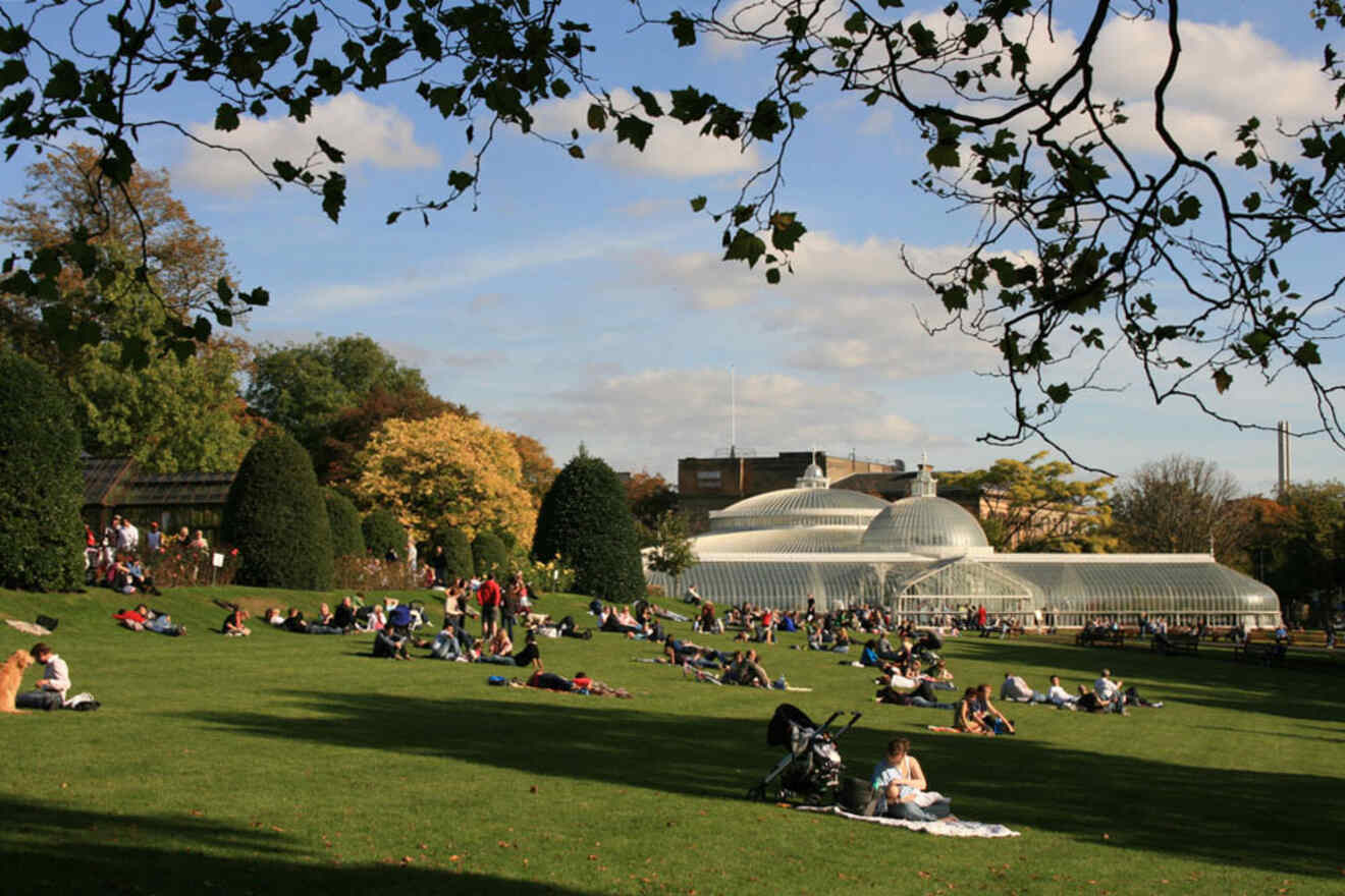 Relaxed atmosphere in Glasgow's West End, with people lounging on the grass in front of the iconic glasshouse, illustrating a budget-friendly neighborhood