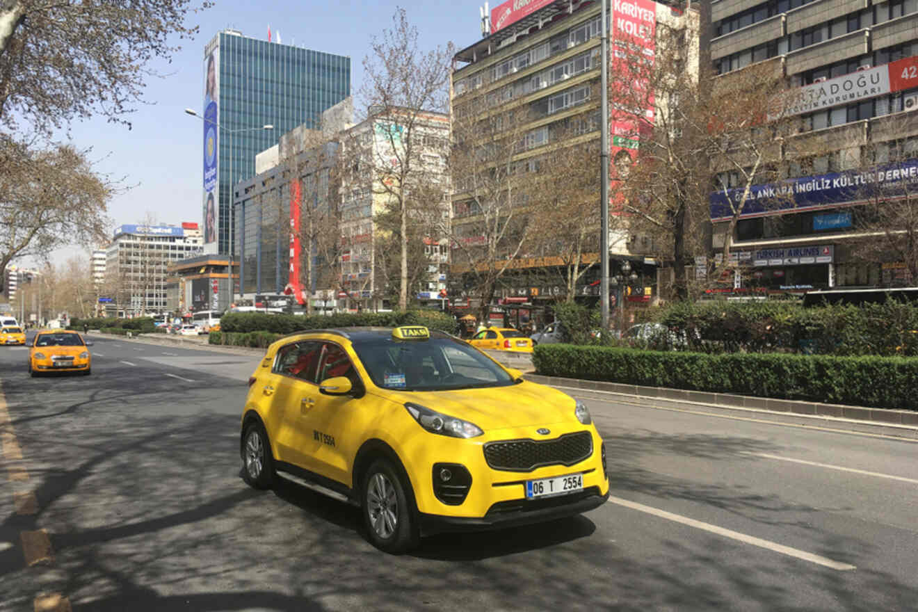 A yellow taxi driving through the busy streets of Ankara with modern buildings and urban life in the background