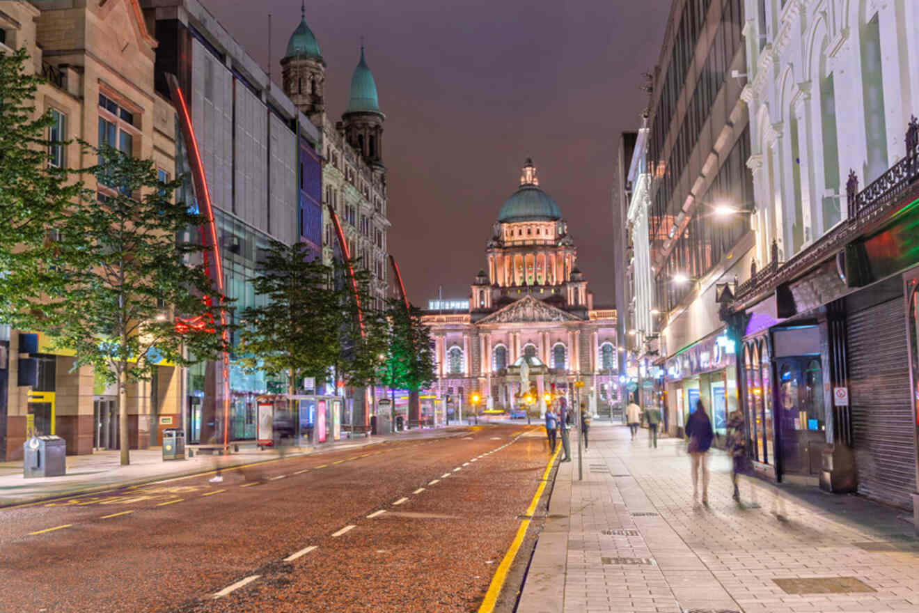 Belfast City Hall illuminated at night, viewed from a vibrant, bustling street.