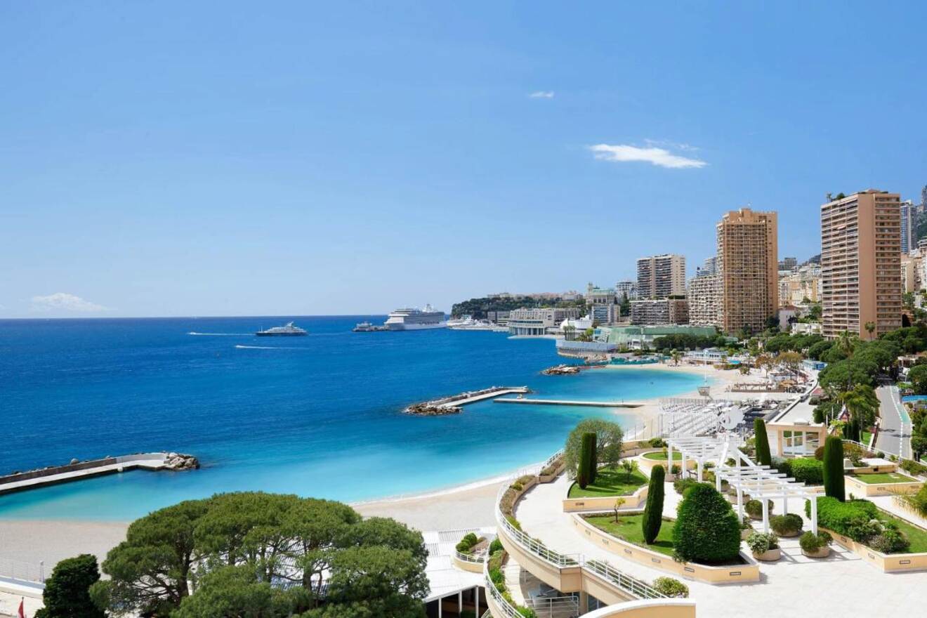 Aerial view of Larvotto Beach with its clear turquoise waters, white sandy shore, and a backdrop of Monaco's urban landscape