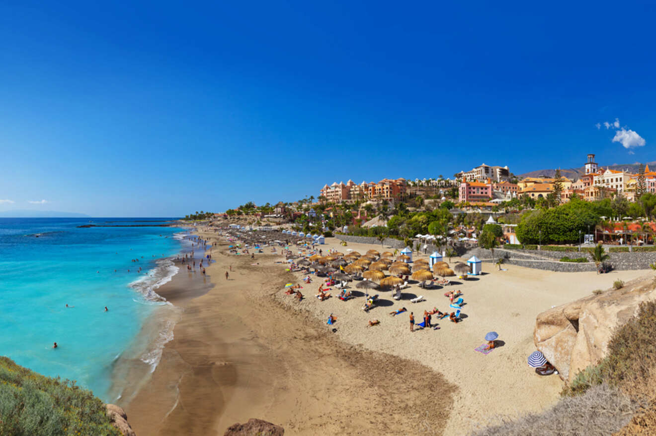 Sweeping view of Playa de las Américas beach with sunbathers, azure waters, and beachfront resorts set against a backdrop of clear blue sky