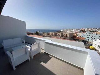 White patio furniture on a balcony with a seaside town view