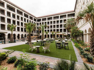 Tranquil courtyard inside Estancia del Norte with green lawn, surrounding balcony access, and outdoor seating.