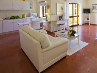 Comfortable living room with a large white sofa, an open-plan kitchen and dining area in the background