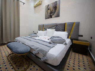Modern bedroom with a sleek gray headboard, accentuated with yellow throw pillows, and classic Moroccan tiled flooring
